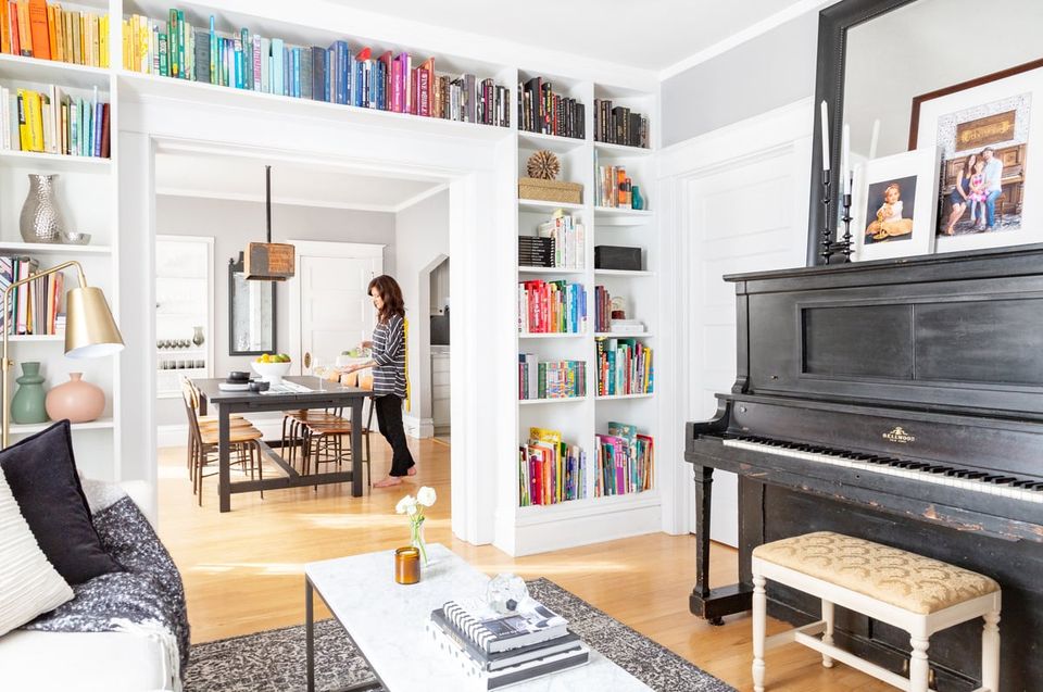 Nostalgic living room with white built-in bookshelves, black grand piano, and warm wood floors creating a literary, vintage-inspired atmosphere.