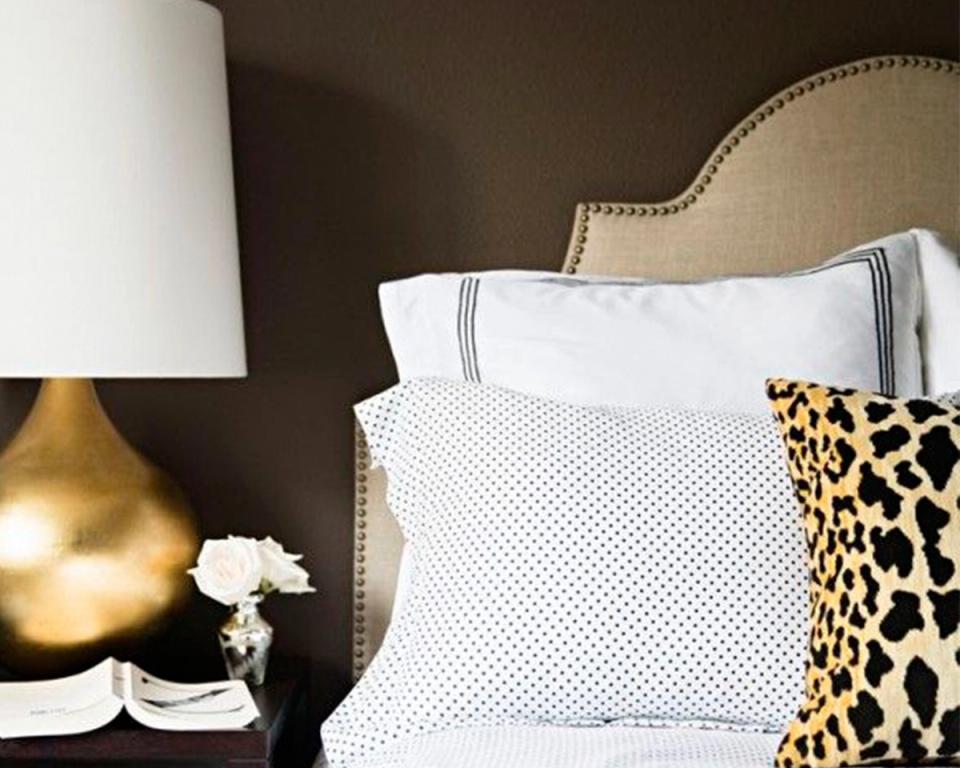 Cozy bedroom nook with dark walls, neutral upholstered headboard, layered white bedding, and bold leopard print accent pillow