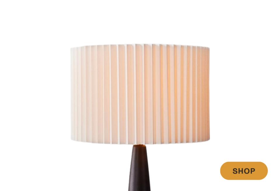 Warm pleated linen drum shade on dark tapered base, soft ambient lighting aesthetic