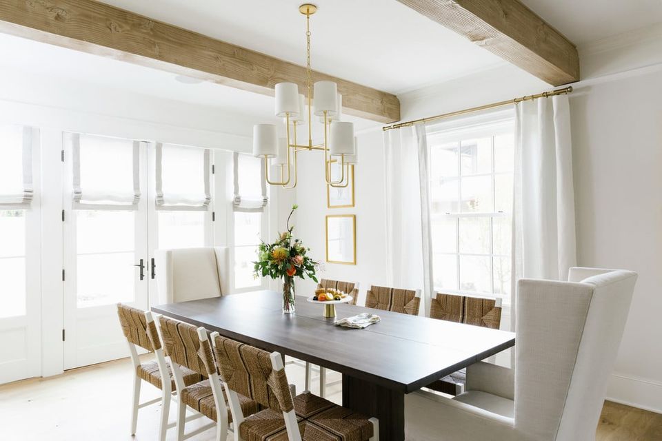 Transitional dining room with black table, woven chairs, brass pendant lighting, and rustic wood beams