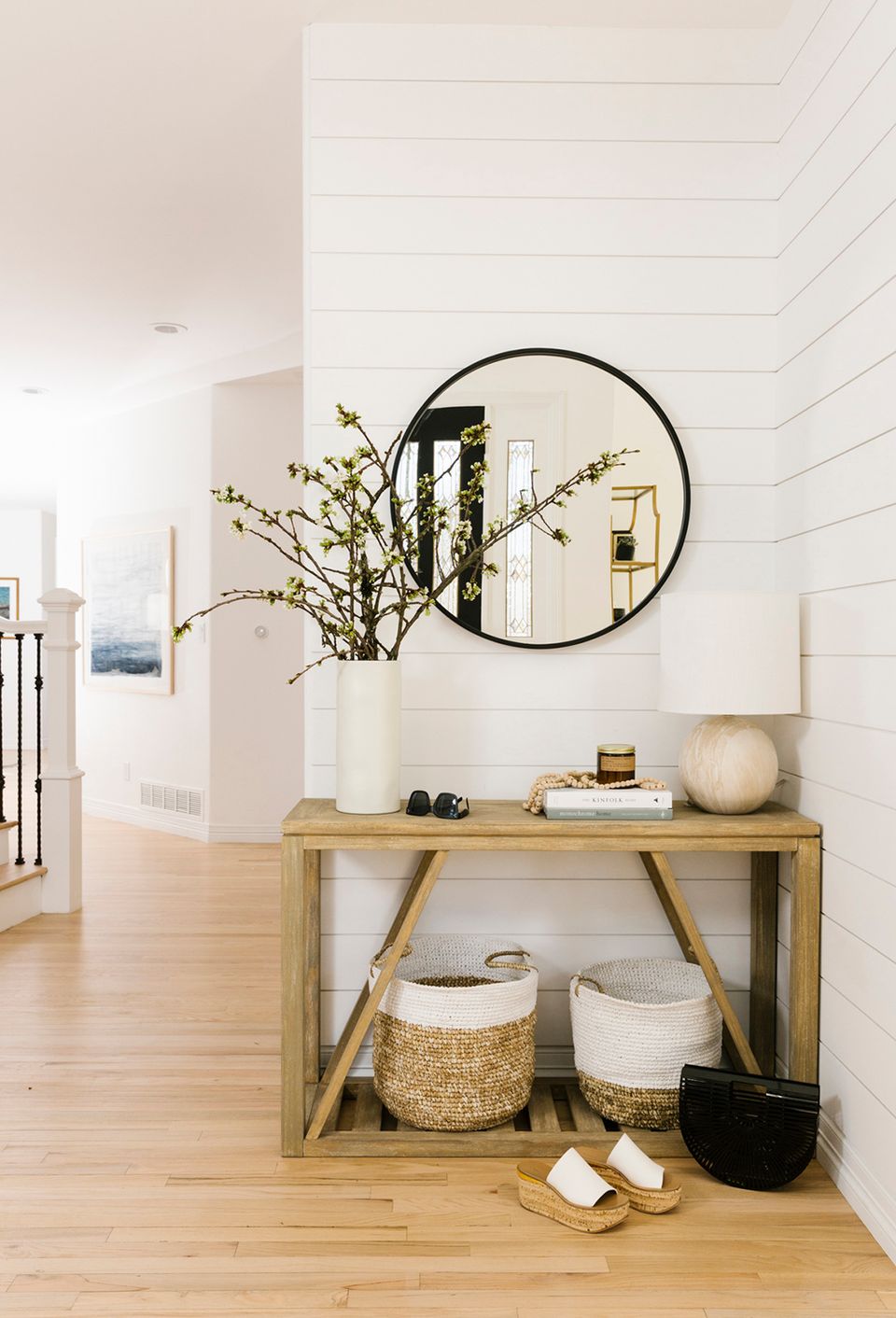 Modern farmhouse entryway with natural wood console, black round mirror, and coastal simplicity