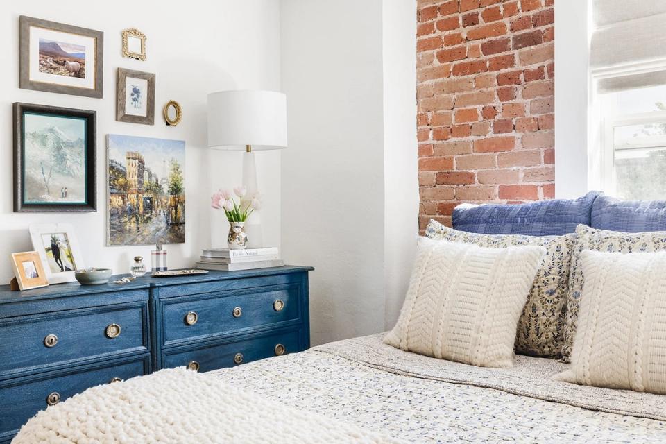 Eclectic bedroom blending industrial blue dresser with exposed brick and gallery wall art