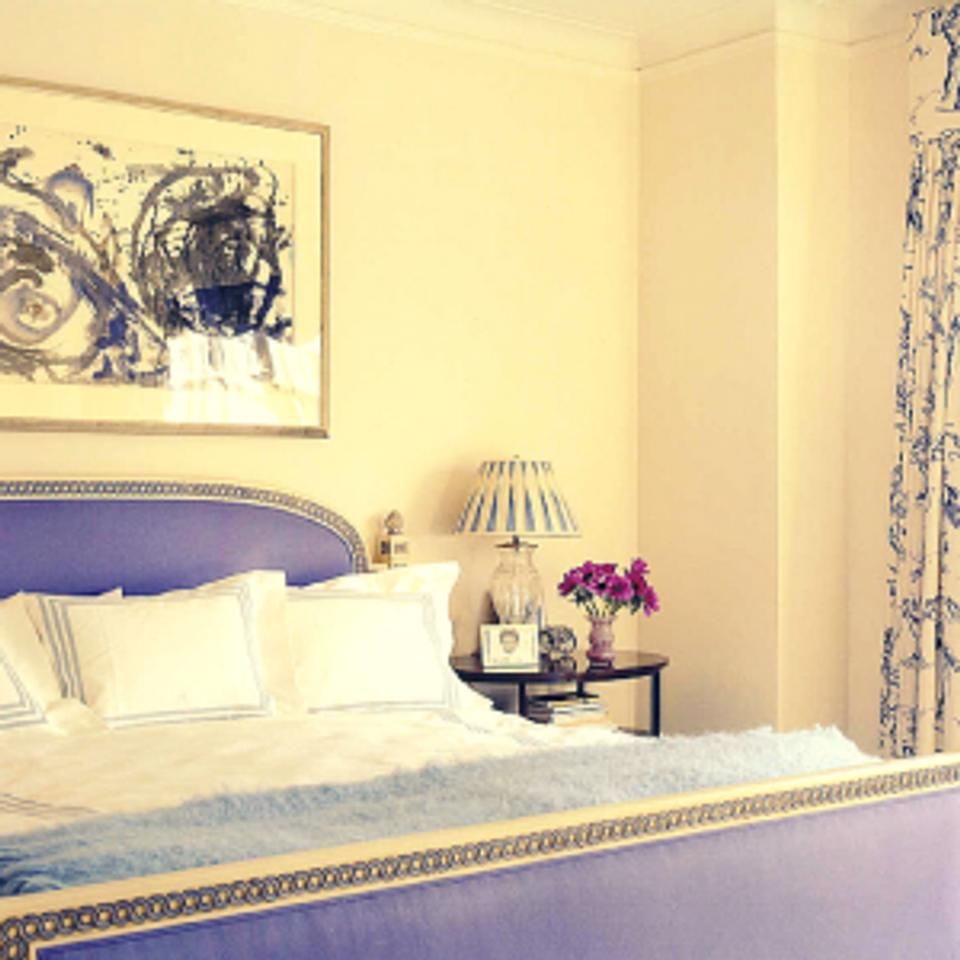Serene bedroom: soft yellow walls, navy upholstered headboard, cream bedding, and blue-white florals