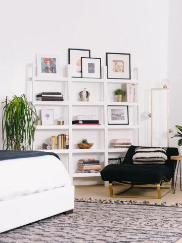 Scandinavian-inspired bedroom featuring white modular wall shelving, black accent bench, and neutral palette with botanical accents and curated décor.