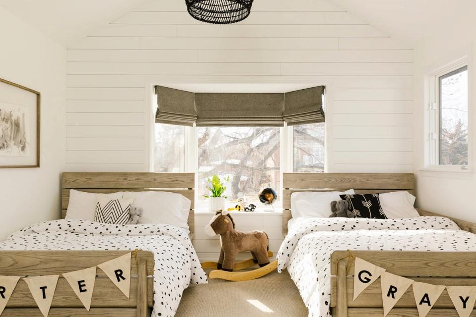 Rustic farmhouse boys' bedroom with dual twin beds, natural wood frames, cream shiplap walls, and vintage-inspired bunting flags creating a shared, cozy retreat.