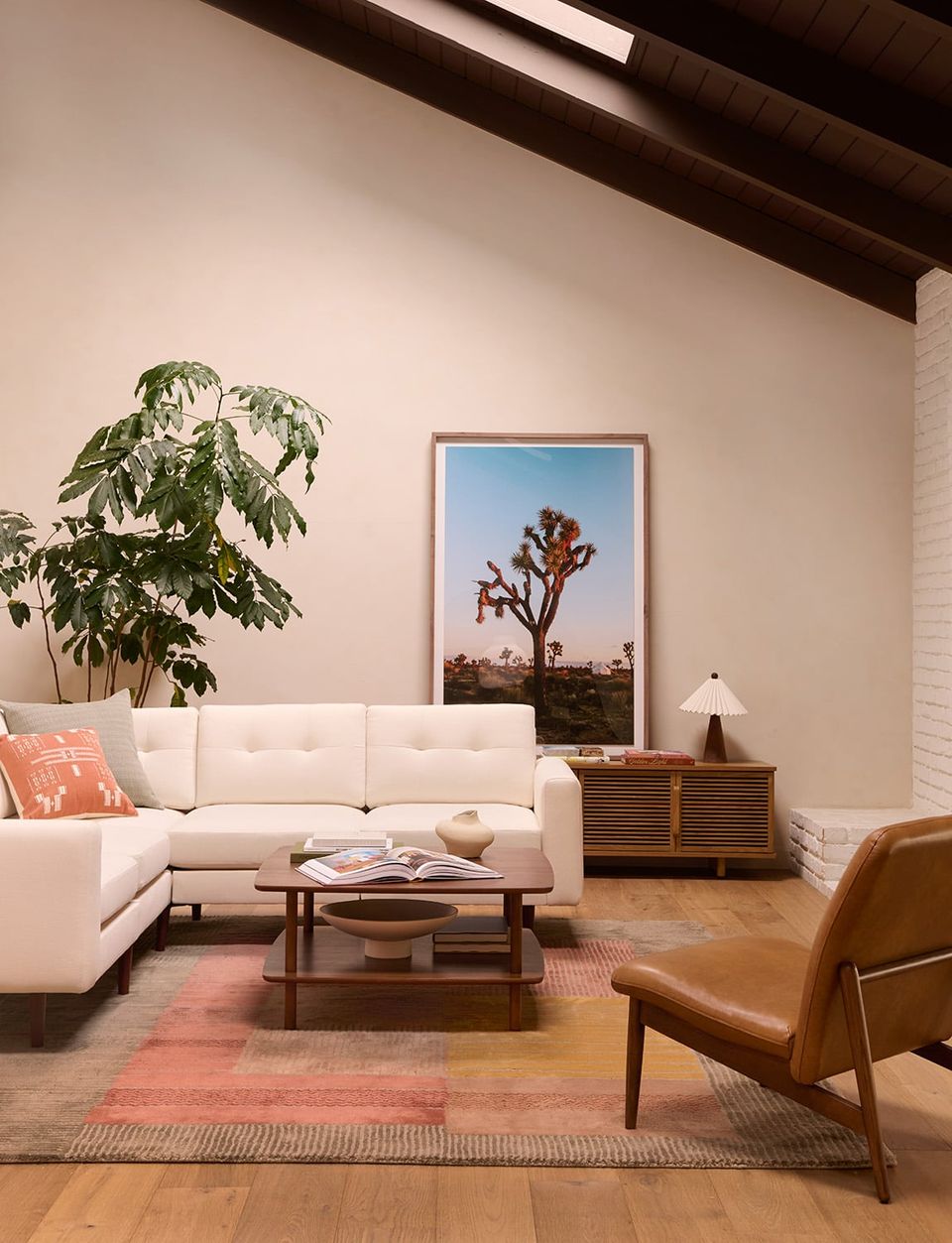 Mid-century modern living room featuring cream sectional, warm wood furniture, and terracotta-toned layered rugs