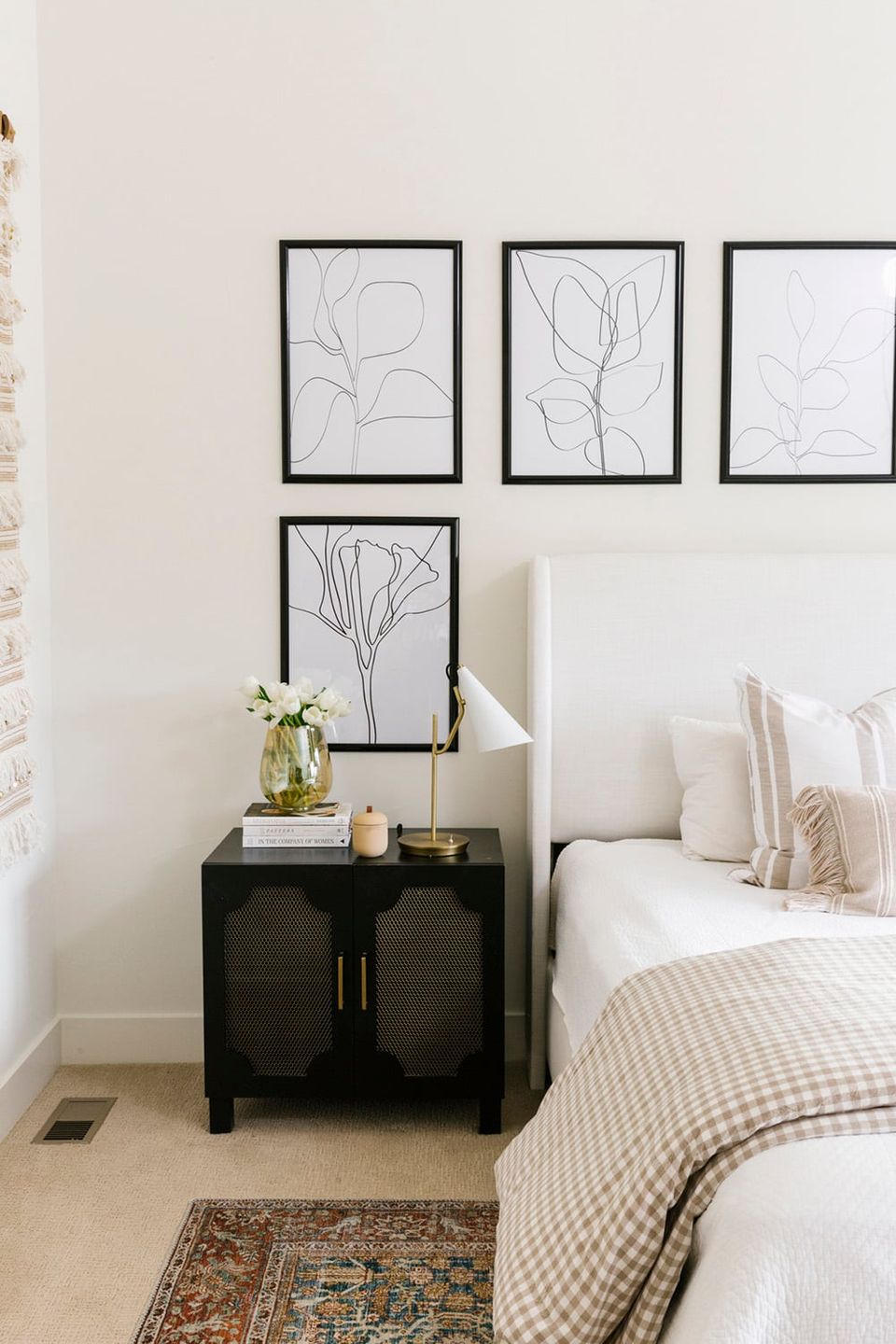 Contemporary bedroom with minimalist black framed botanical line art, black nightstand, and soft neutral bedding creating a calm, modern sanctuary.