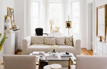 Bright transitional living room with cream sofa, gold accents, and floor-to-ceiling windows creating an airy, sophisticated atmosphere.