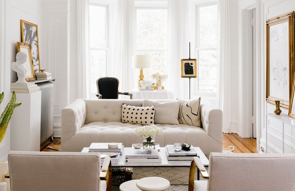 Bright transitional living room with cream sofa, gold accents, and floor-to-ceiling windows creating an airy, sophisticated atmosphere.