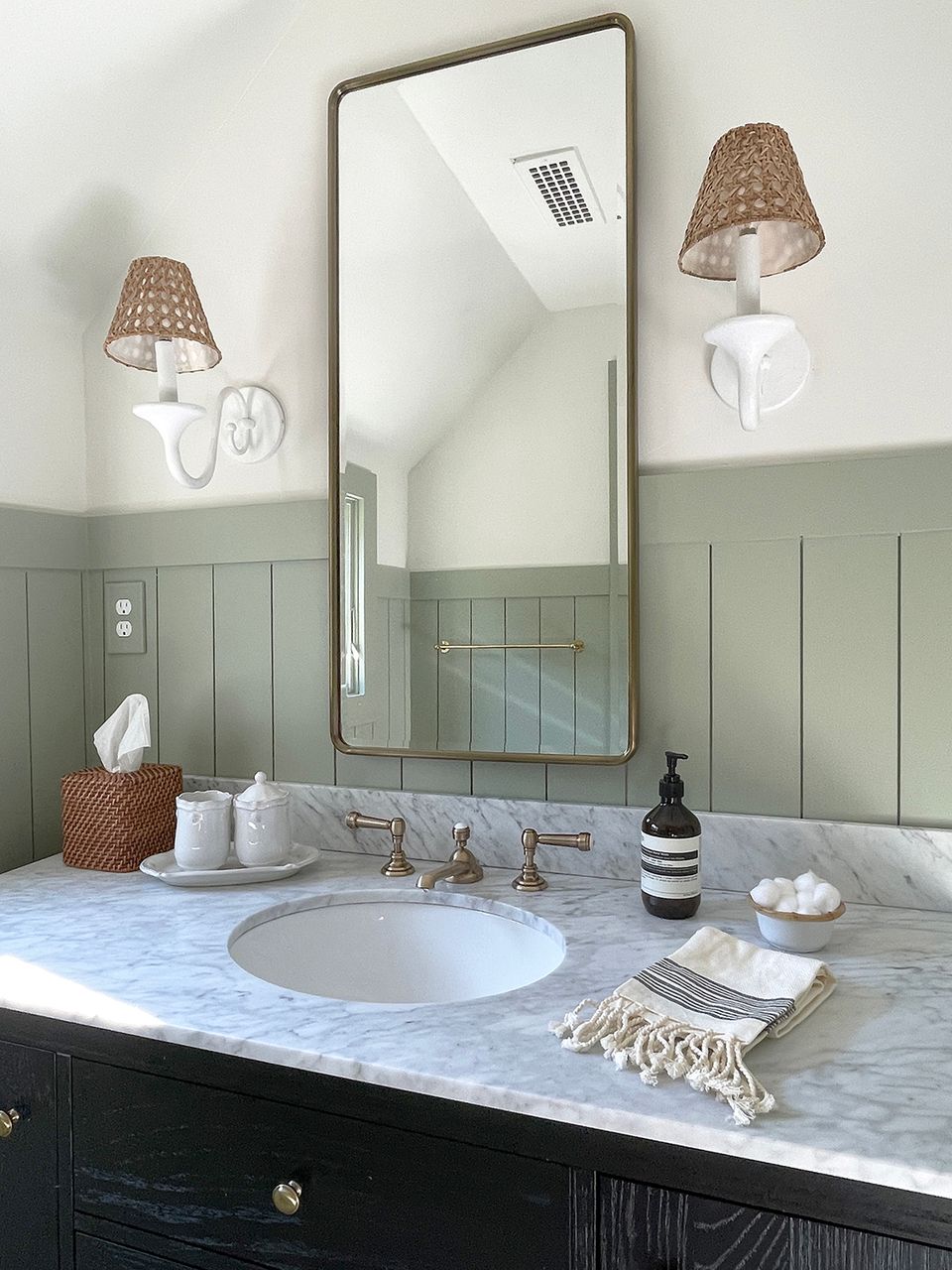 Tranquil vanity detail with marble countertop, large mirror, woven lampshades, and soft brass hardware