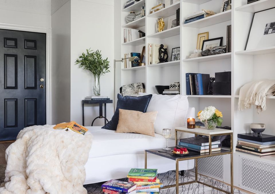 Bright, minimalist bedroom with floor-to-ceiling white shelving displaying curated books and decor in neutral tones