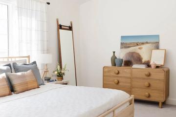Serene mid-century bedroom with warm wood furniture, soft neutral palette, and curated gallery wall creating calm, collected aesthetic