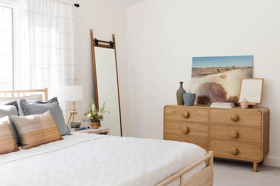 Serene mid-century bedroom with warm wood furniture, soft neutral palette, and curated gallery wall creating calm, collected aesthetic