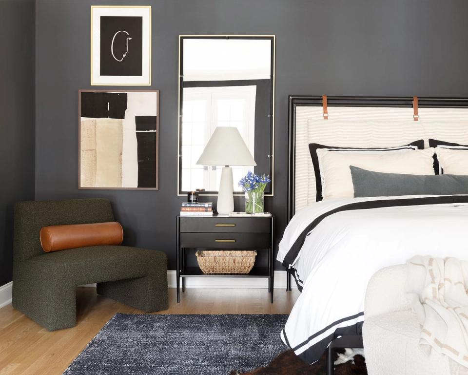 Moody charcoal bedroom with crisp white bedding, leather accents, and gallery wall styling