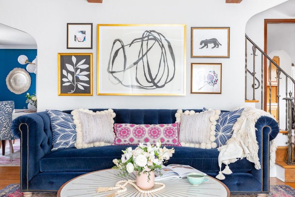 Eclectic living room with navy velvet sofa, gallery wall art, white accents, and warm wood tones creating a sophisticated bohemian aesthetic.