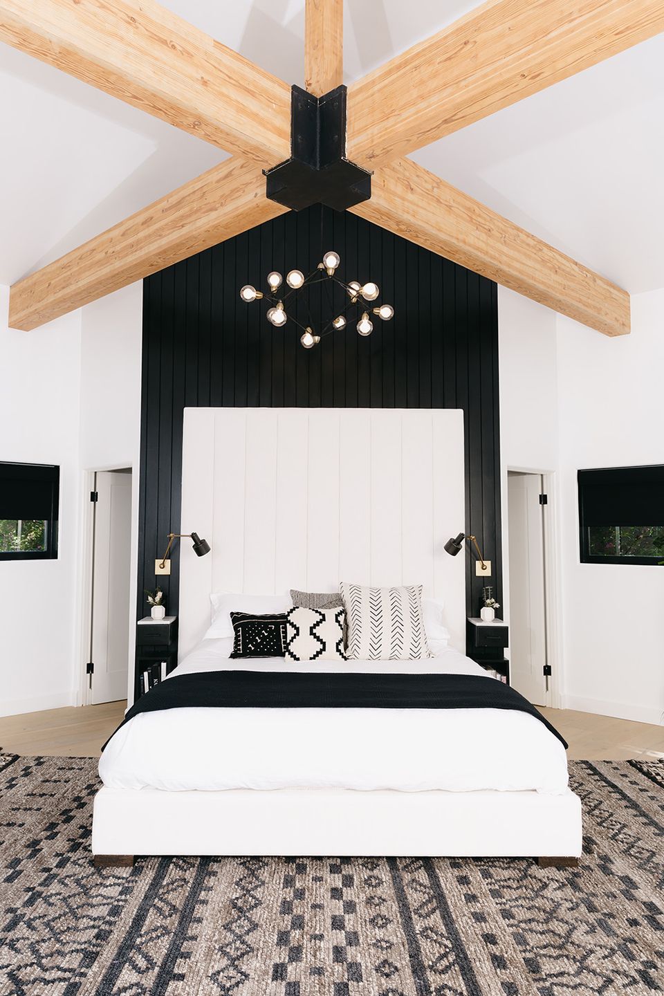 Modern farmhouse bedroom with black accent wall, exposed wood ceiling beams, and crisp white bedding
