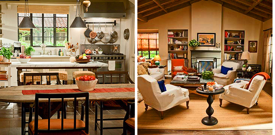 Warm cottage kitchen with black cabinetry and wood island beside cozy living room with cream chairs and fireplace.
