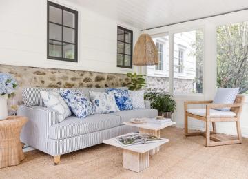 Bright transitional sunroom with blue striped sofa, natural wood accents, and soft striped rug creating an airy, coastal feel.