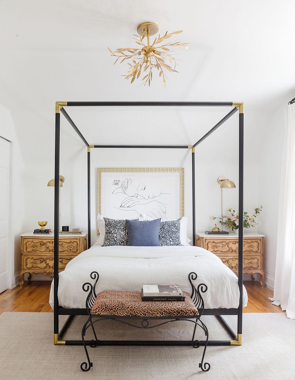 Contemporary canopy bed with black metal frame, gold accents, natural wood nightstands, and airy white palette