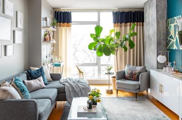 Eclectic small living room with teal accent wall, layered textiles, warm wood tones, and abundant natural light from large windows