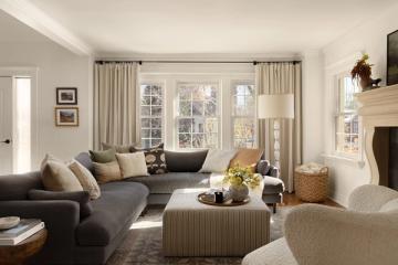 Neutral contemporary living room with charcoal sectional, warm taupe accents, and natural light from large windows