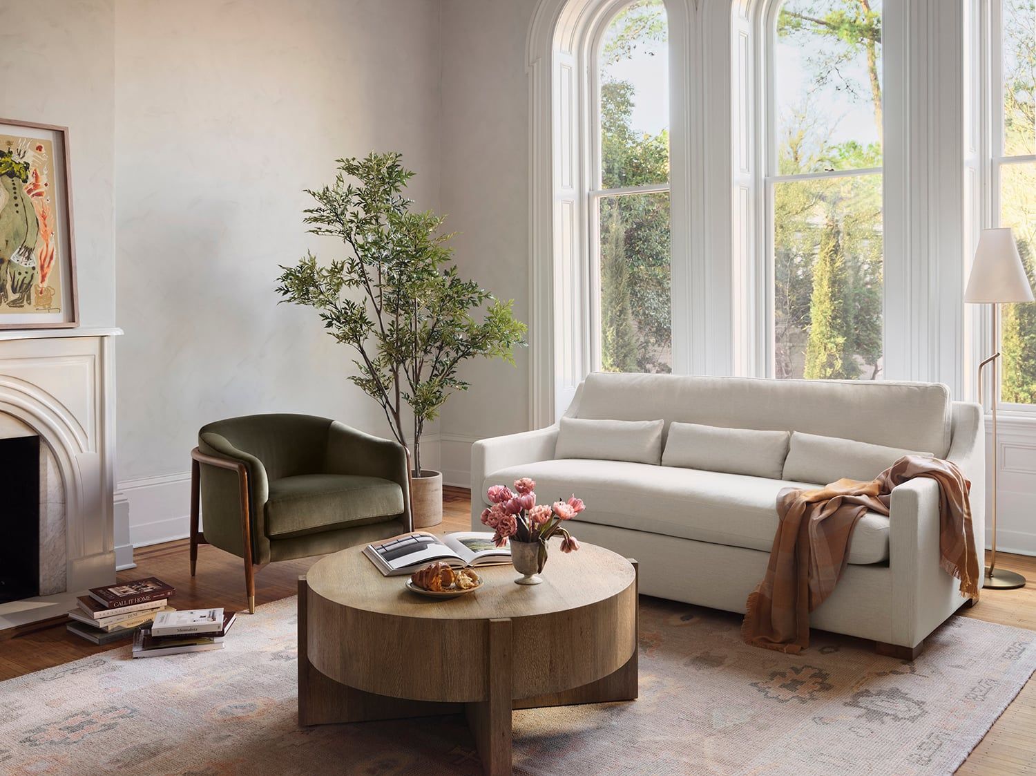 Warm, contemporary living room with neutral palette, round wood coffee table, and lush greenery