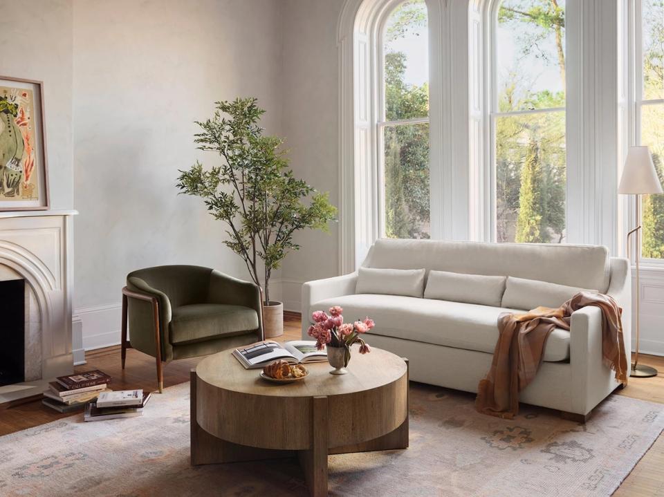 Warm, contemporary living room with neutral palette, round wood coffee table, and lush greenery