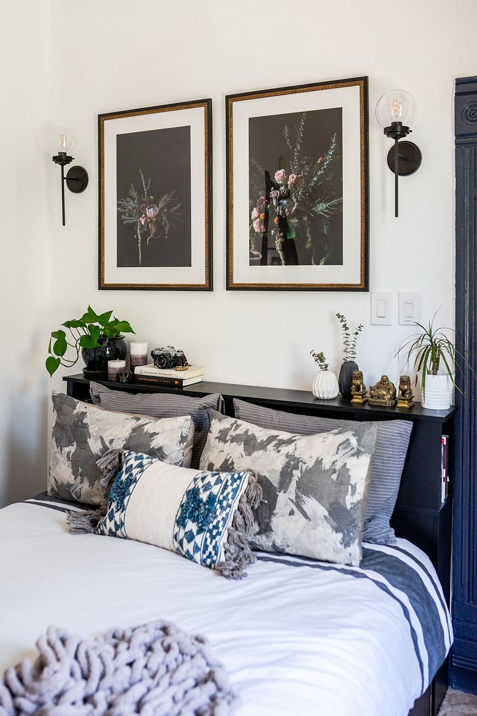 Serene bedroom with botanical artwork, sculptural sconces, neutral palette, and styled nightstand creating peaceful, nature-inspired retreat.