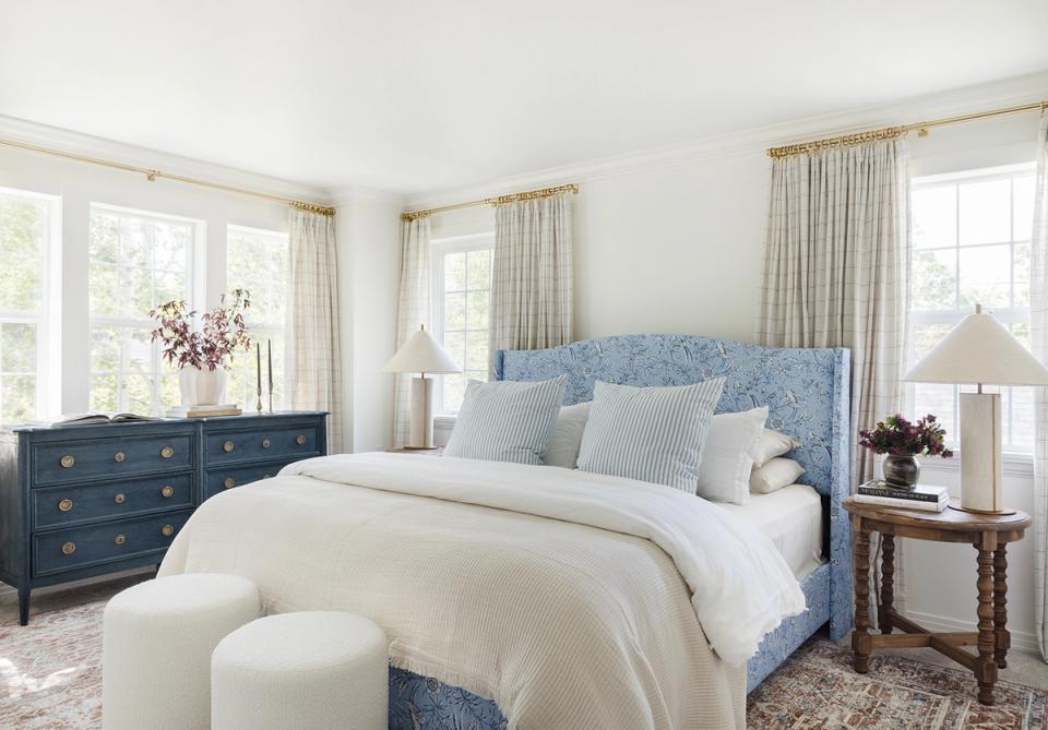 Serene coastal bedroom with soft blue upholstered headboard, cream bedding, and warm wood furnishings creating a calming, unified atmosphere