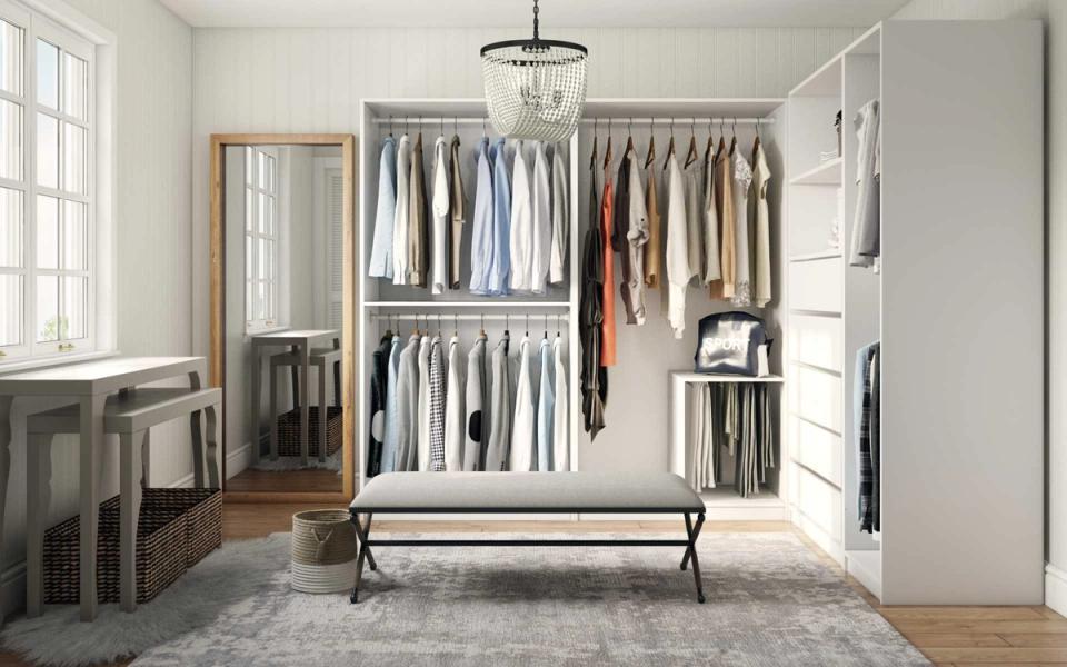Minimalist closet with organized neutral clothing on metal rods, white shelving, and industrial bench in bright, airy space
