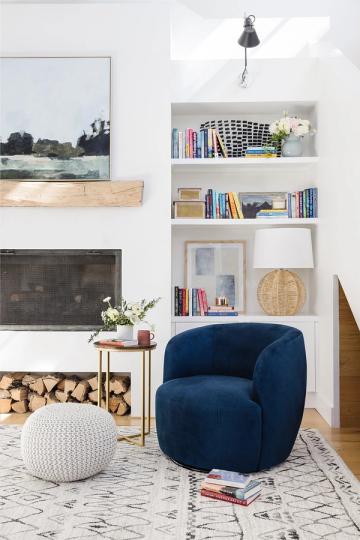 Modern living room with white built-in shelves, navy curved chair, coastal artwork, and warm wood storage details