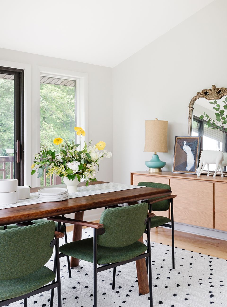 Mid-century modern dining room with warm wood table, green chairs, fresh florals, and soft neutral palette accented by turquoise ceramic pieces