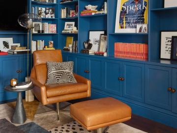 Bold cobalt blue built-in shelving with warm cognac leather chair and geometric pillows