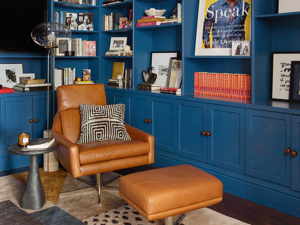 Bold cobalt blue built-in shelving with warm cognac leather chair and geometric pillows