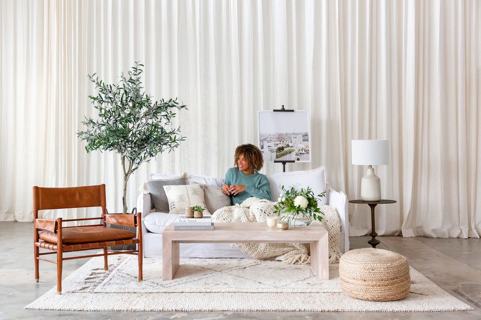 Scandinavian living room with warm wood furniture, neutral palette, flowing white curtains, and natural greenery creating a calm, minimalist aesthetic.
