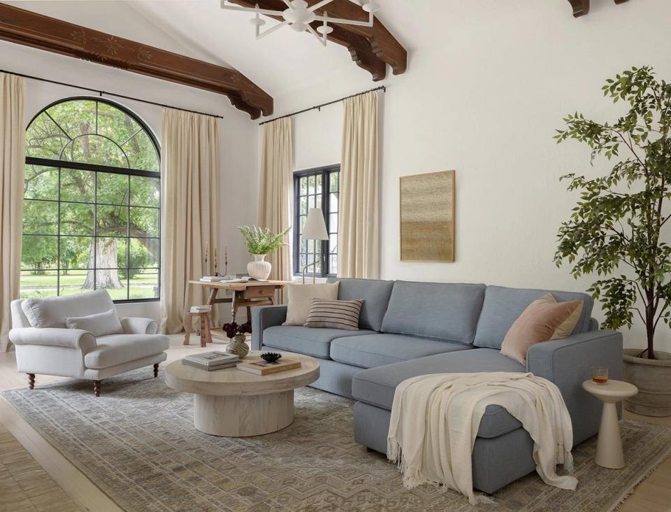 Transitional living space with slate blue sofa, exposed wood beams, cream drapery, and organic botanical styling