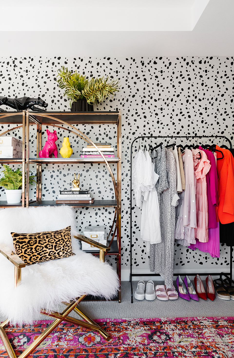 Eclectic bedroom with bold polka-dot wallpaper, colorful clothing rack, leopard chair, and vibrant layered rug for playful energy.