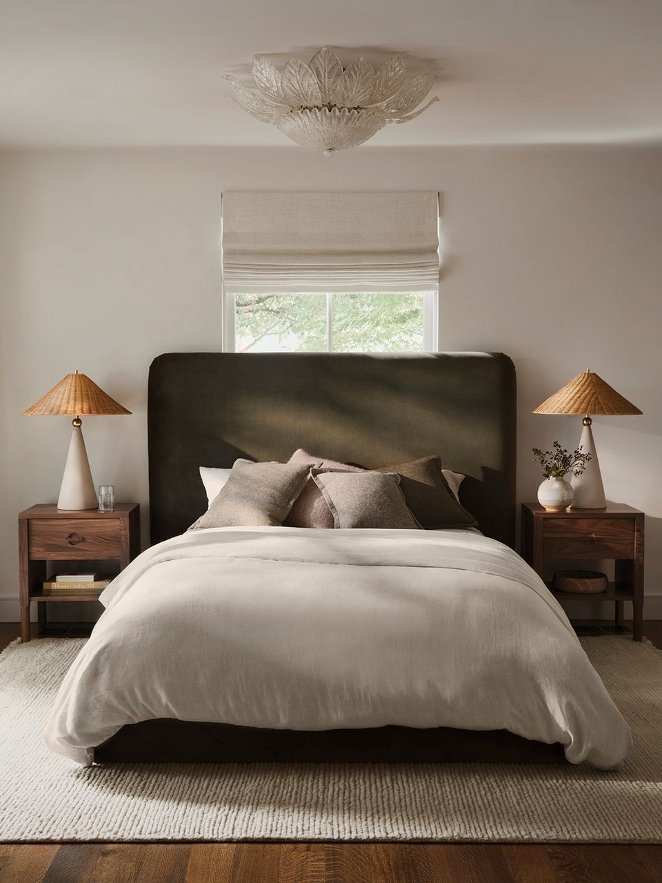 Contemporary boho bedroom with dark upholstered headboard, cream linens, and warm wood nightstands