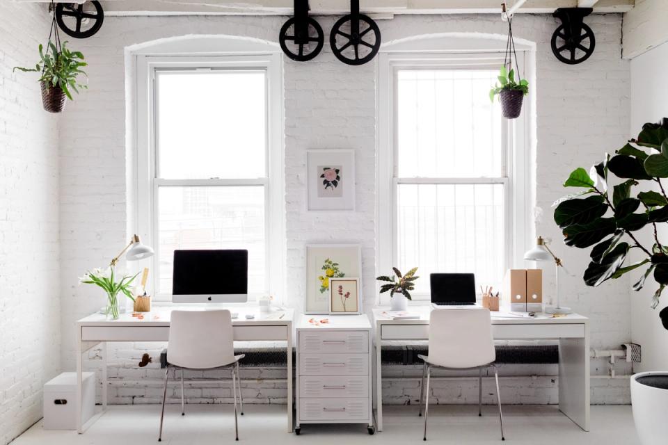 Minimalist dual-desk home office with whitewashed wood, potted plants, and industrial black pendant lights creating balanced, calming feng shui.