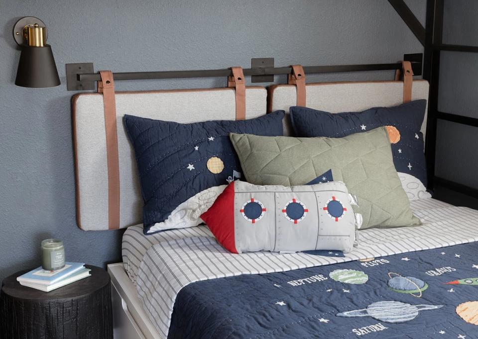 Contemporary boy's bedroom with industrial metal bed frame, navy and sage bedding, geometric patterns, and moody gray walls creating a sophisticated yet playful atmosphere.