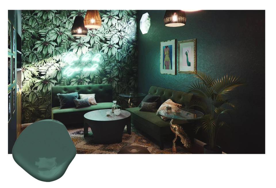 Moody living room with dark forest green walls, tropical leaf wallpaper feature, charcoal seating, and ambient pendant lighting evoking a jungle-inspired sanctuary