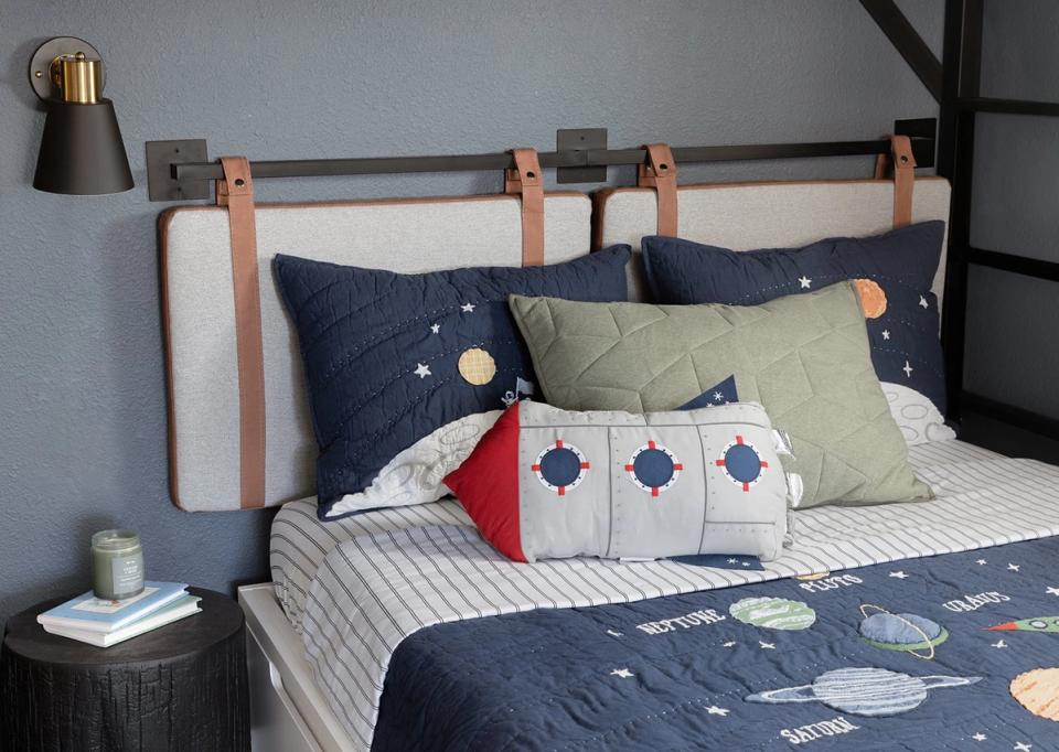 Modern bedroom with navy and sage bedding, leather headboard, and playful space-themed accents