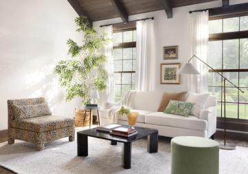Scandinavian-inspired room with light green ottoman, cream sofa, natural textures, and large windows creating peaceful minimalist ambiance