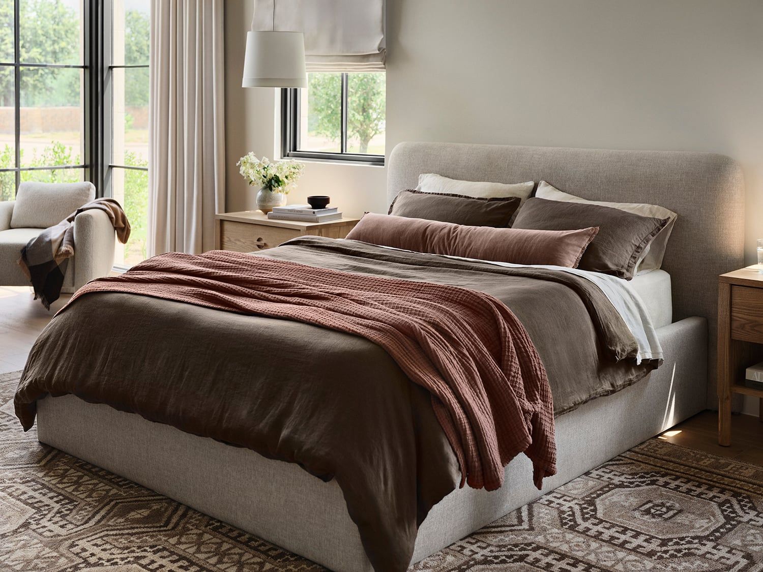 Serene primary bedroom with warm burgundy tones, neutral upholstered bed, and soft natural light from expansive windows