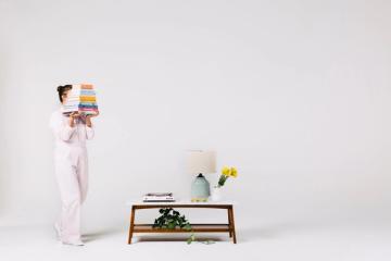 Minimalist interior with woman holding paint samples beside mid-century modern wooden console table with plants and flowers