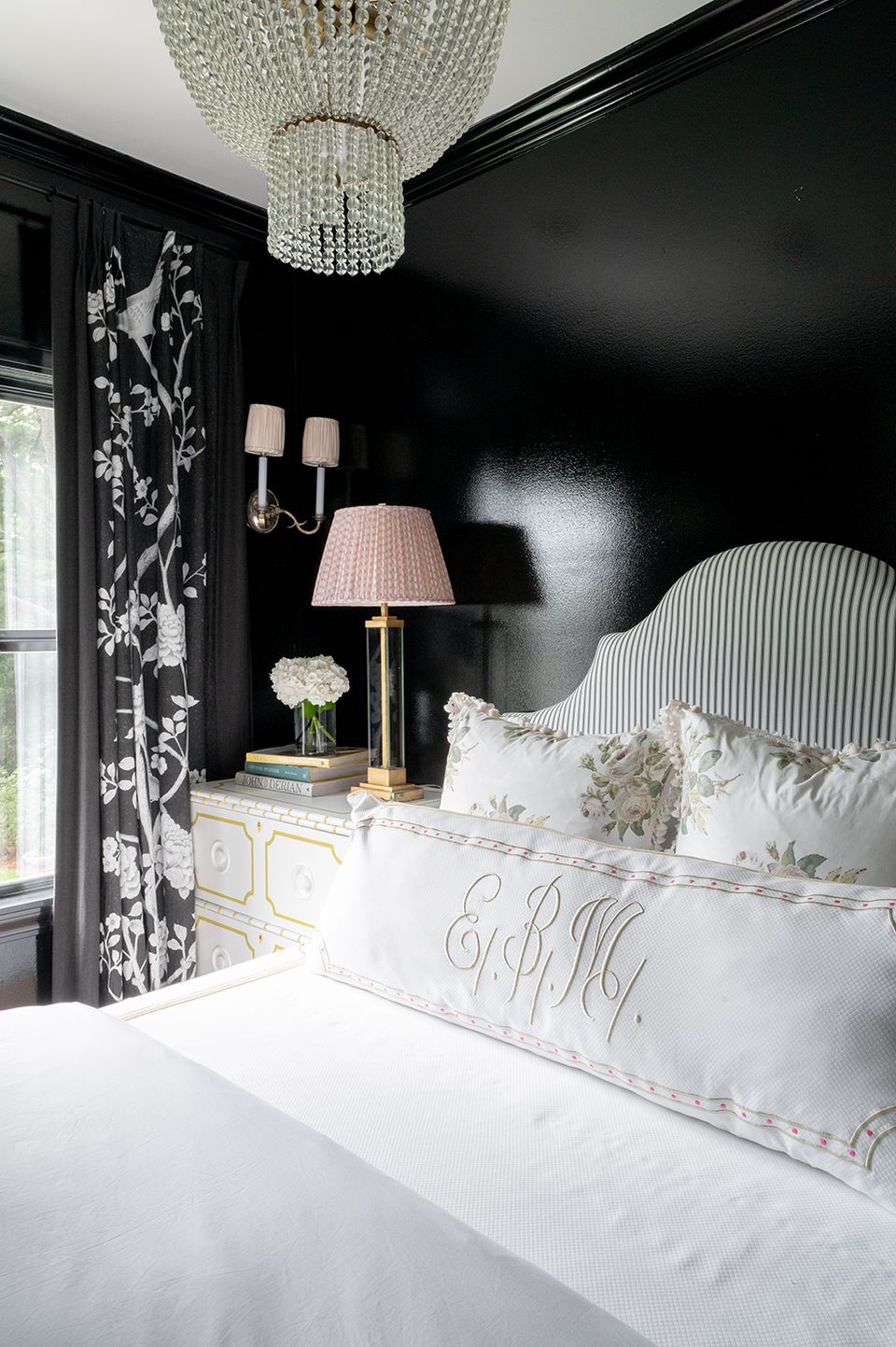 Glamorous bedroom with black walls, crystal chandelier, black floral curtains, and monochromatic bedding