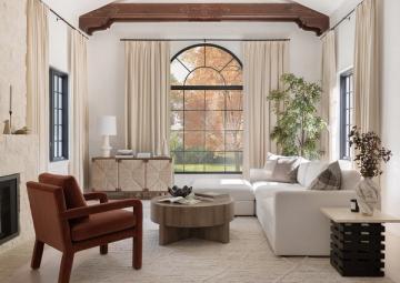 Transitional living room with cream tones, cognac leather chair, white sofa, and arched window framed by drapery