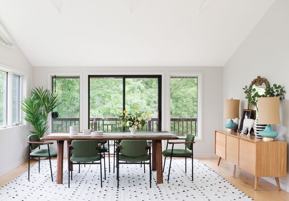 Mid-century dining area with wood table, green chairs, and serene forest views through expansive windows