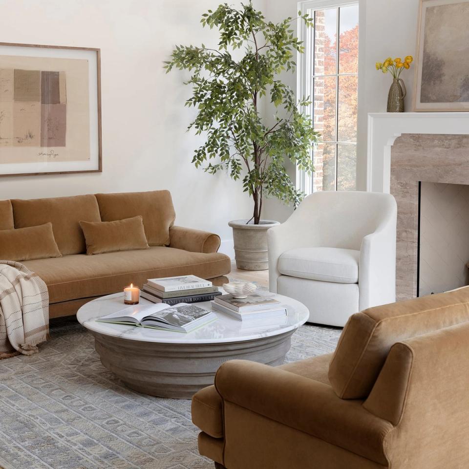 Contemporary living room blending caramel and cream upholstery with white marble round table and greenery against light walls