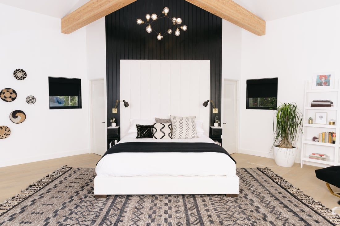 Modern bedroom with scandinavian minimalism: black accent wall, natural wood beam, geometric patterned rug, pendant lights